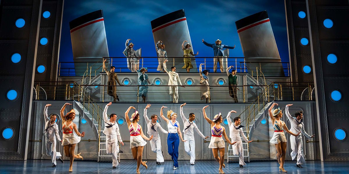 Ensemble cast of Anything Goes dancing energetically in colourful costumes on stage.