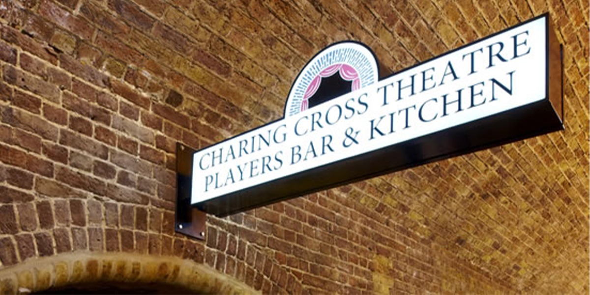A sign reading 'Charing Cross Theatre Players Bar & Kitchen' against a brick wall.