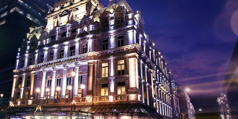 A grand theatre facade with red brick walls, featuring ornate architectural details against a clear blue sky.