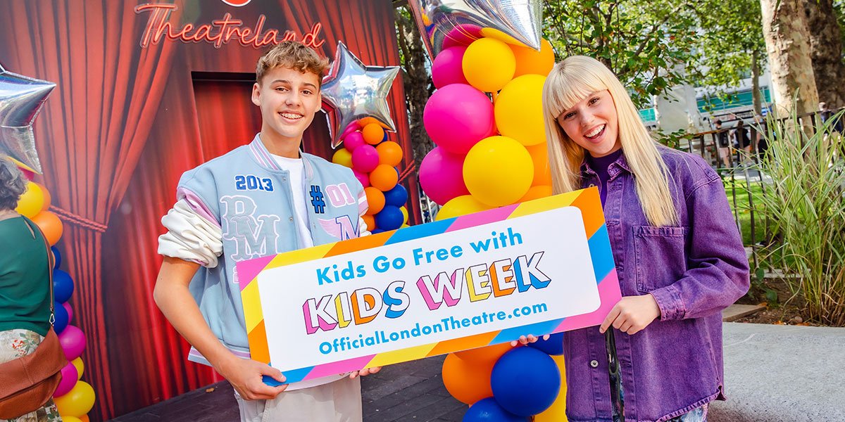 Two kids stand either side of a sign saying 'Kids go free with Kids Week'