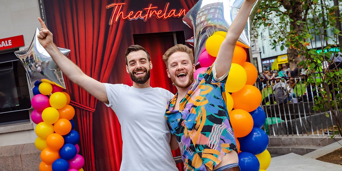 Two people stand with their arms outstretched, one wearing a white tshirt, one wearing a colourful shirt