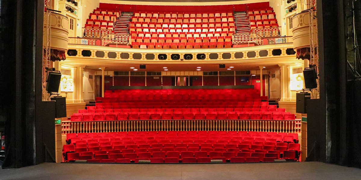 The auditorium of Theatre Royal Windsor, showcasing red velvet seats, intricate gold decorations, and a grand stage.